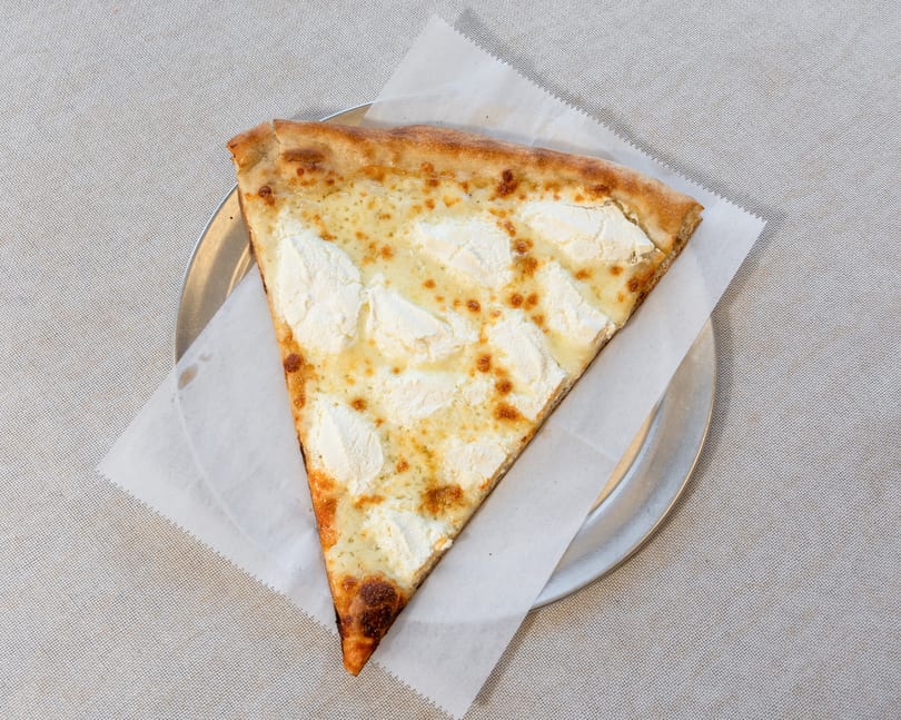 A single slice of white pizza with ricotta cheese and golden crust on a metal plate.