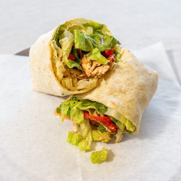 A chicken wrap, cut in half, filled with lettuce, red peppers, and chicken, on white paper.