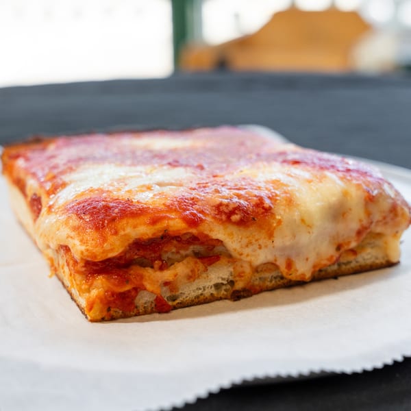Thick square slice of Detroit-style pizza with melted cheese and red sauce on parchment paper.