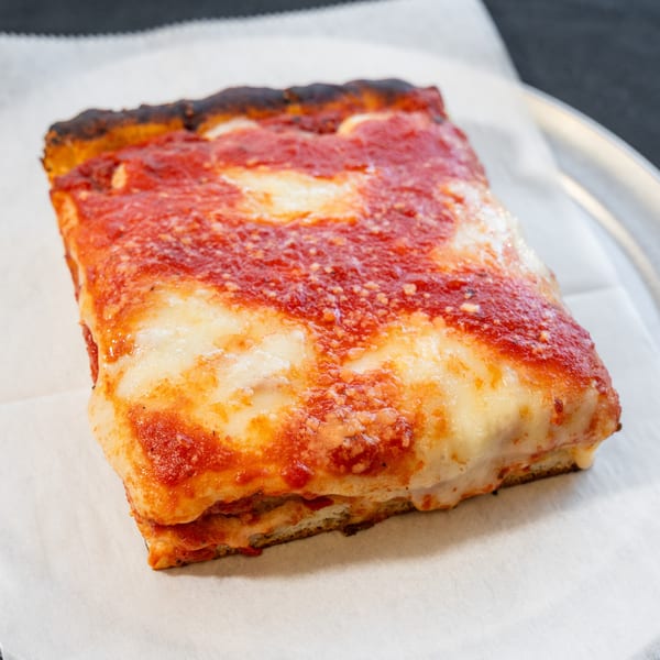 A thick square slice of Detroit-style pizza with melted cheese and red sauce on parchment paper.