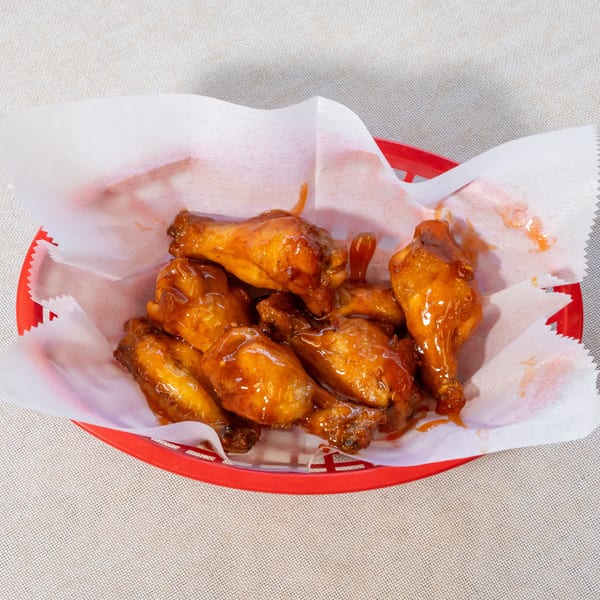 A red plastic basket filled with several glistening, saucy chicken wings on white parchment paper.