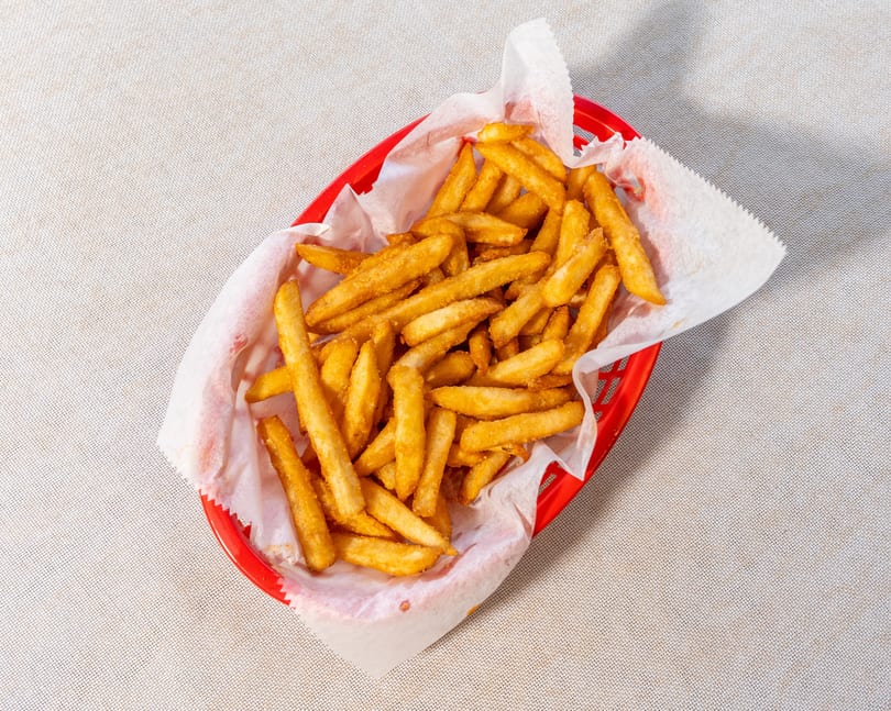 Golden brown french fries in a red plastic basket lined with white paper.