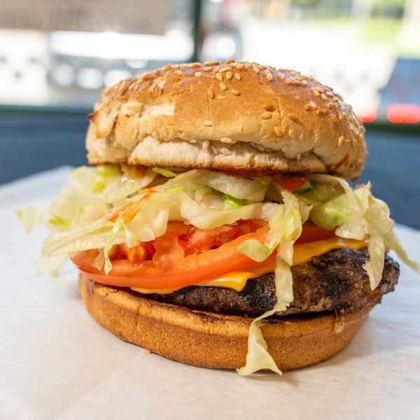 A close-up of a cheeseburger with lettuce, tomato, and sauce on a sesame seed bun.