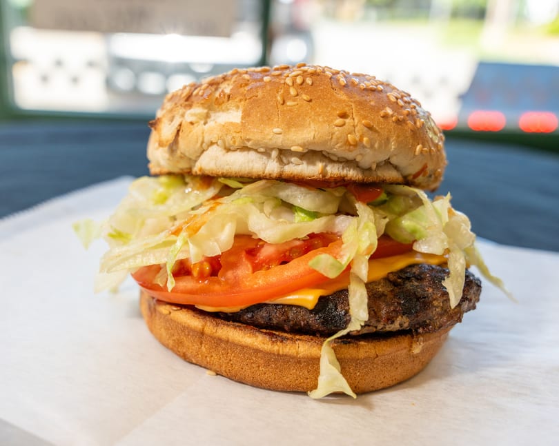 A close-up of a cheeseburger with lettuce, tomato, and sauce on a sesame seed bun.