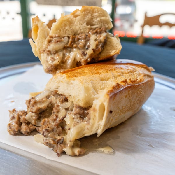 A sliced cheesesteak sandwich with melted cheese and onions on a white paper-lined tray.