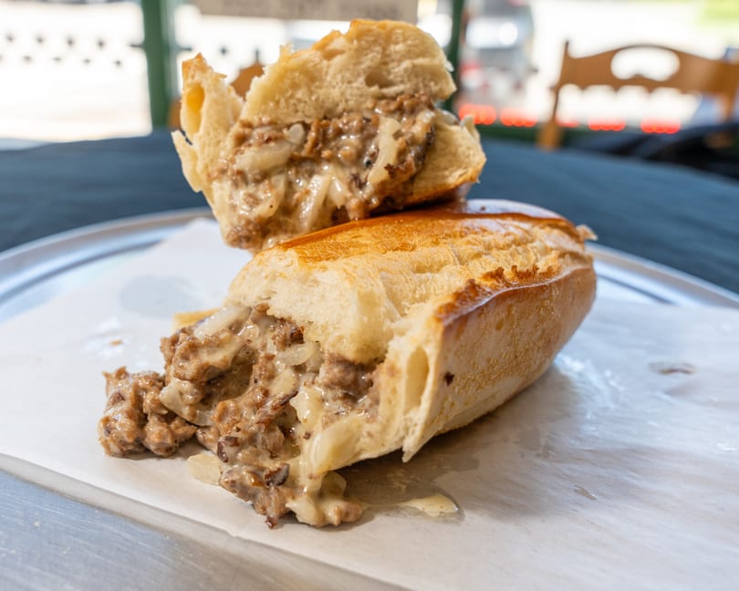A sliced cheesesteak sandwich with melted cheese and onions on a white paper-lined tray.