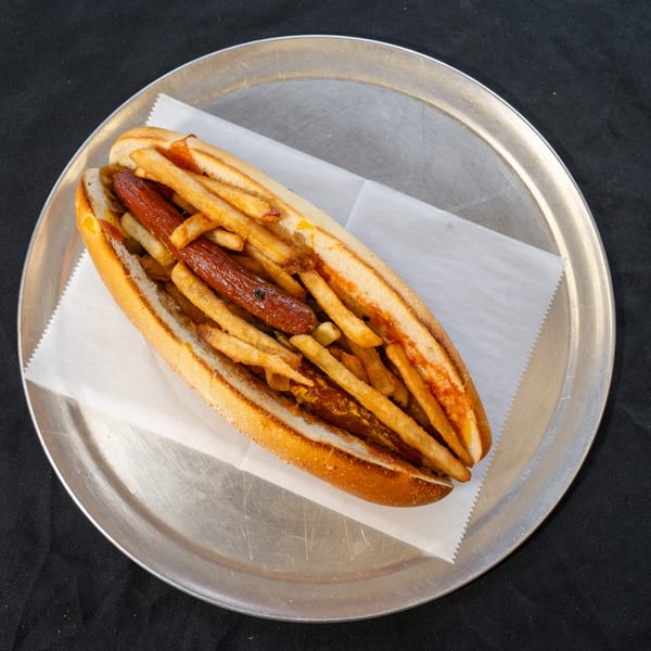 Hot dog with fries and mustard in a bun, served on a metal plate.