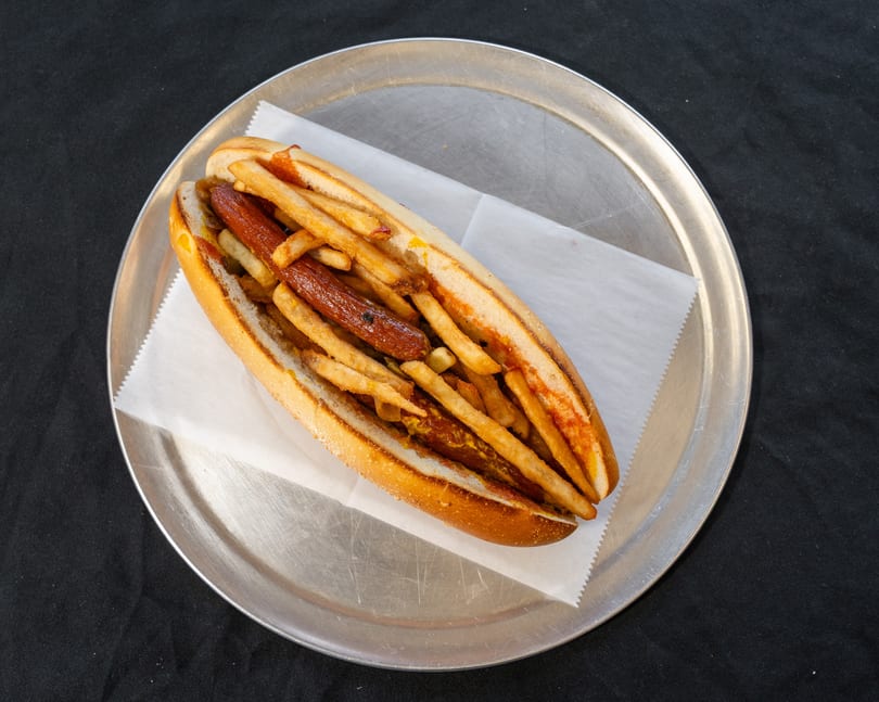 Hot dog with fries and mustard in a bun, served on a metal plate.