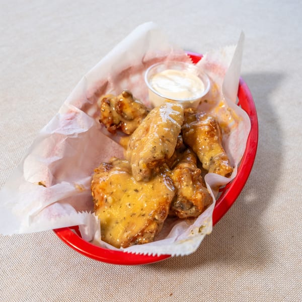 A red basket of chicken wings coated in a creamy sauce, with a side of dipping sauce.
