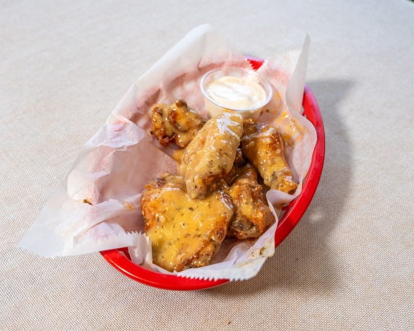 A red basket of chicken wings coated in a creamy sauce, with a side of dipping sauce.