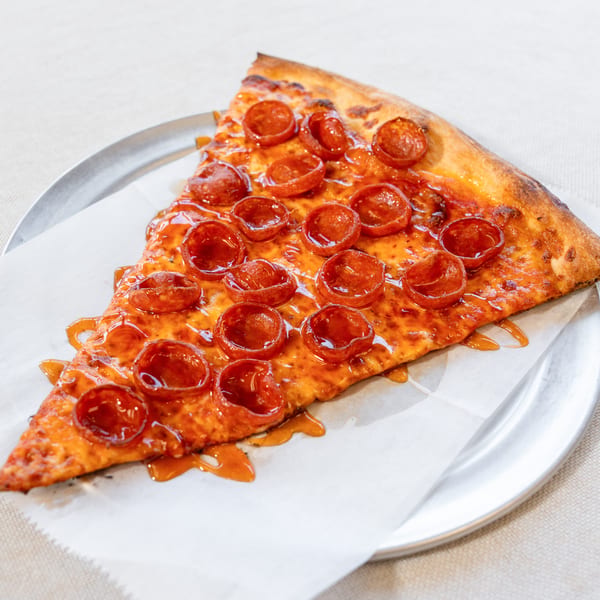 A single slice of pepperoni pizza, drizzled with hot honey, rests on a metal plate.