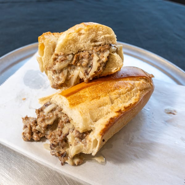 A cheesesteak sandwich, cut in half, filled with meat, onions, and melted cheese on a metal tray.