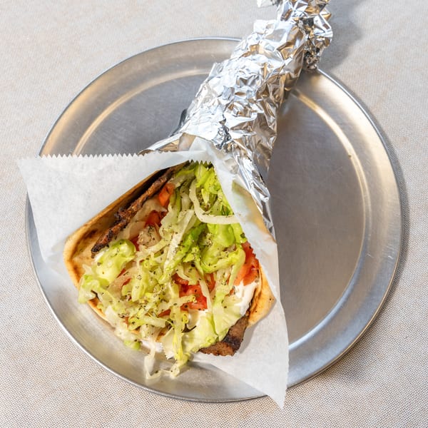 A gyro with meat, lettuce, tomatoes, and sauce, partially wrapped in foil on a metal plate.