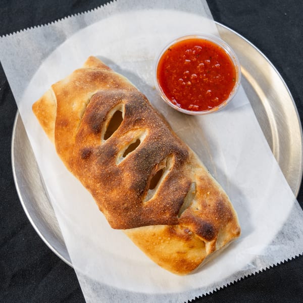 Golden-brown calzone with slits on top, served with a side of red marinara sauce on a metal plate.