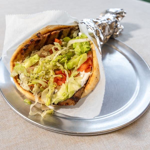 A gyro with meat, lettuce, tomatoes, and white sauce, partially wrapped in foil on a metal plate.