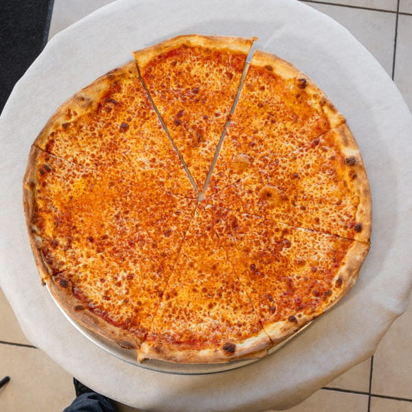 A large, round cheese pizza with two slices removed, on a metal tray atop a white tablecloth.