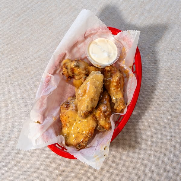 A red basket of saucy chicken wings with a side of ranch dressing on a light-colored tablecloth.