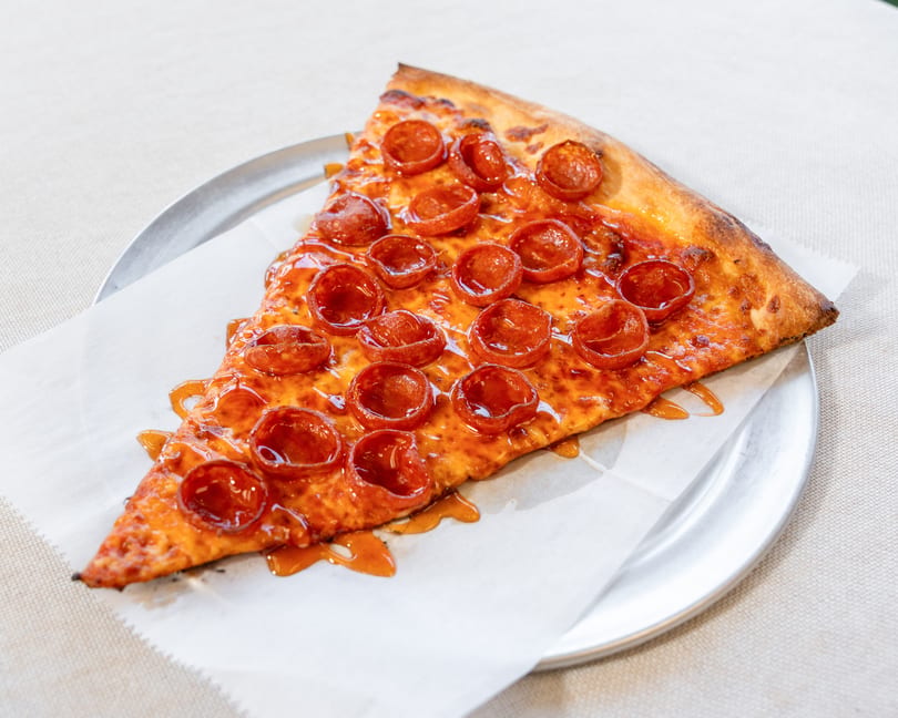 A slice of pepperoni pizza with hot honey drizzle on a metal plate with parchment paper.
