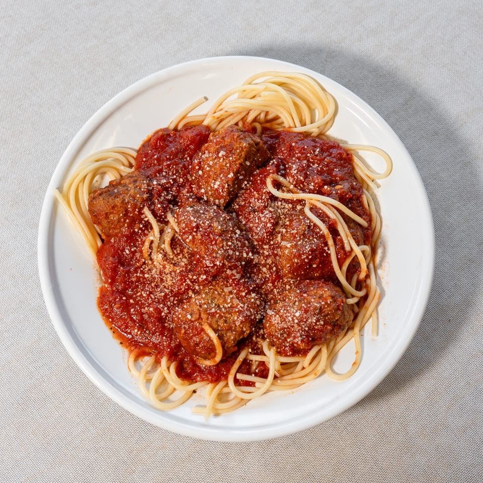 Spaghetti with meatballs and tomato sauce, topped with grated Parmesan cheese on a white plate.