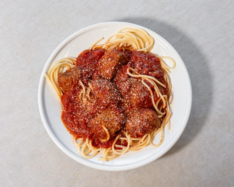Spaghetti with meatballs and tomato sauce, topped with grated Parmesan cheese on a white plate.